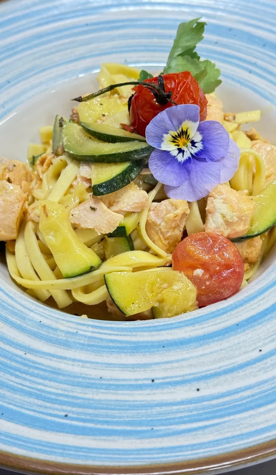 Fettuccine mit Lachs, Zucchini und Kirschtomaten auf blau gestreiftem Teller